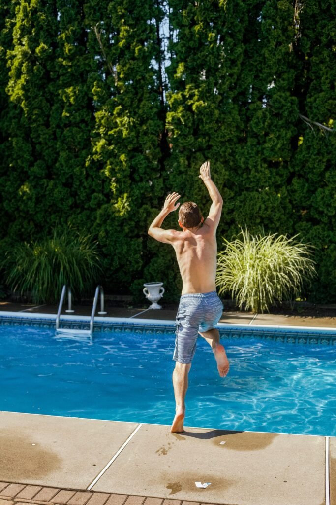 A man enjoying a leap into a vibrant blue swimming pool surrounded by greenery.