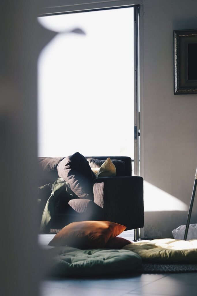 A modern living room illuminated by natural light, featuring a brown sofa and colorful cushions for a cozy atmosphere.